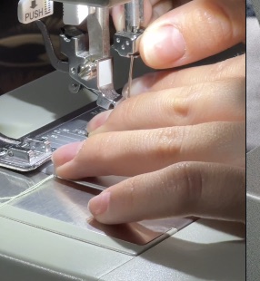 Hands guiding fabric through a gray sewing machine